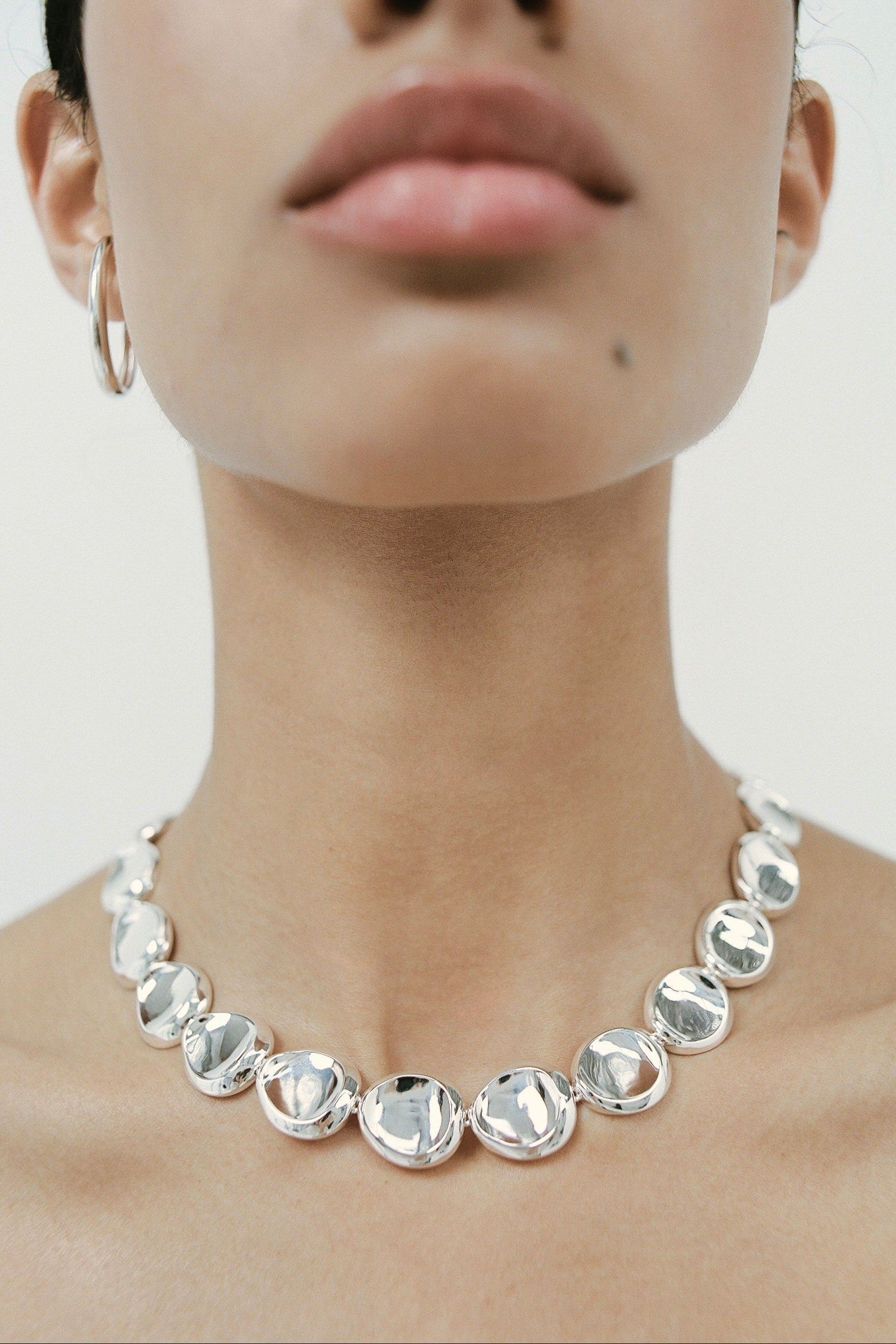 Silver necklace worn by a person on a plain background